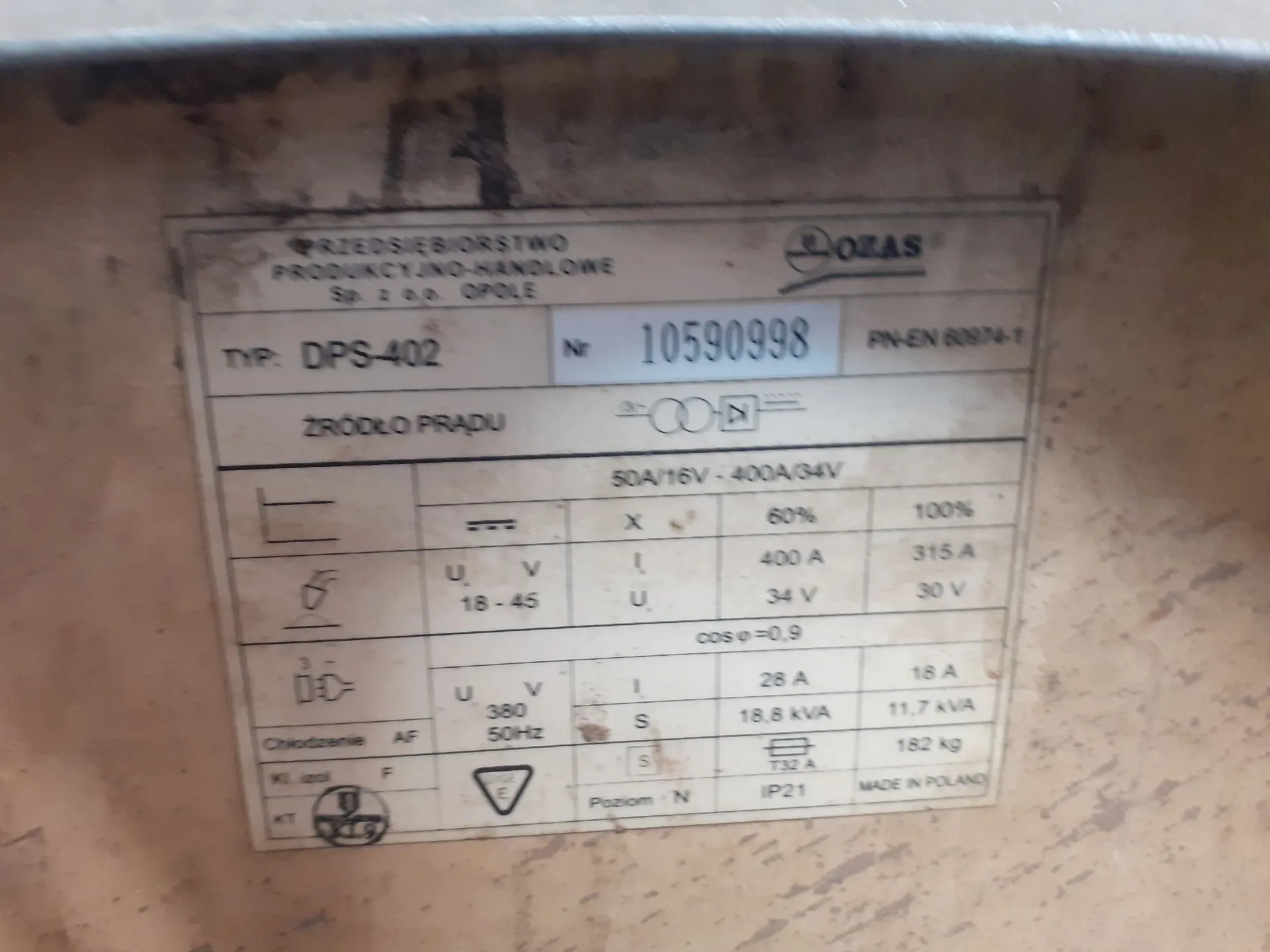 Zdjęcie tabliczki znamionowej urządzenia. Na górze widnieje napis 'PRZEDSIĘBIORSTWO PRODUKCYJNO-HANDLOWE Sp. z o.o. OPOLE' oraz logo 'OZAS'. Poniżej znajduje się typ: 'DPS-402', numer 'Nr 10590998' oraz norma 'PN-EN 60974-1'. Tabliczka zawiera sekcję 'ŹRÓDŁO PRĄDU' z tabelą parametrów technicznych, w tym wartościy prądu i napięcia (np. 50A/16V - 400A/34V), napięcie zasilania '380V 50Hz', moc '18,8 kVA' oraz masę '182 kg'. Na dole widnieje napis 'MADE IN POLAND' oraz stopień ochrony 'IP21'.