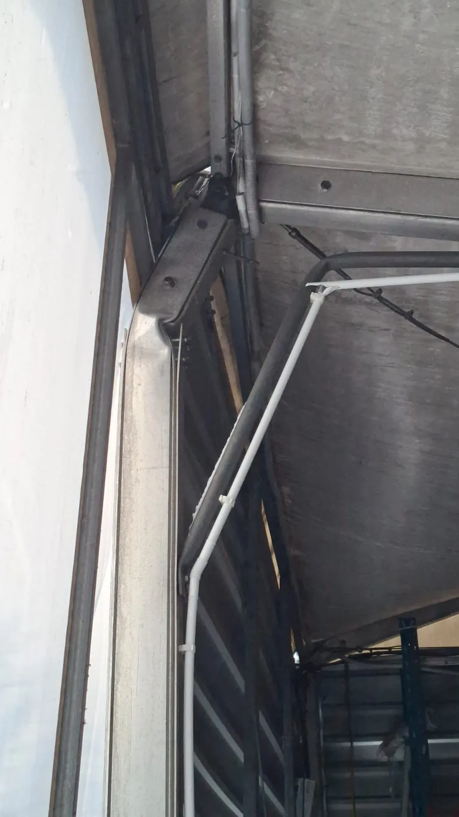 Zbliżenie na metalowe konstrukcje, w tym czarne i białe przewody przymocowane plastikowymi zaciskami. W tle widoczna szara powierzchnia betonowa lub metalowa oraz fragment białej ściany po lewej stronie.