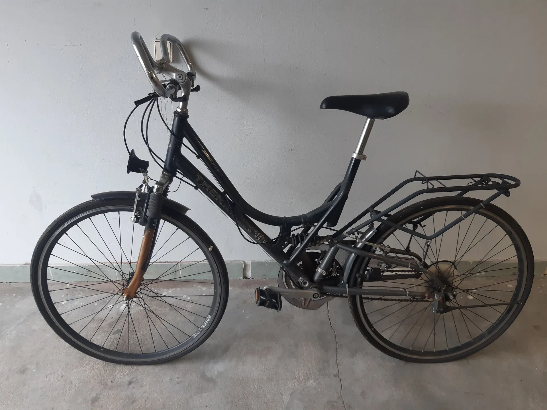 Czarny rower miejski z niską ramą, wyposażony w błotniki, bagażnik z tyłu oraz amortyzator przedniego widelca. Rower stoi bokiem na jasnym tle ściany i podłogi. Na ramie widoczny jest napis 'THORN'.