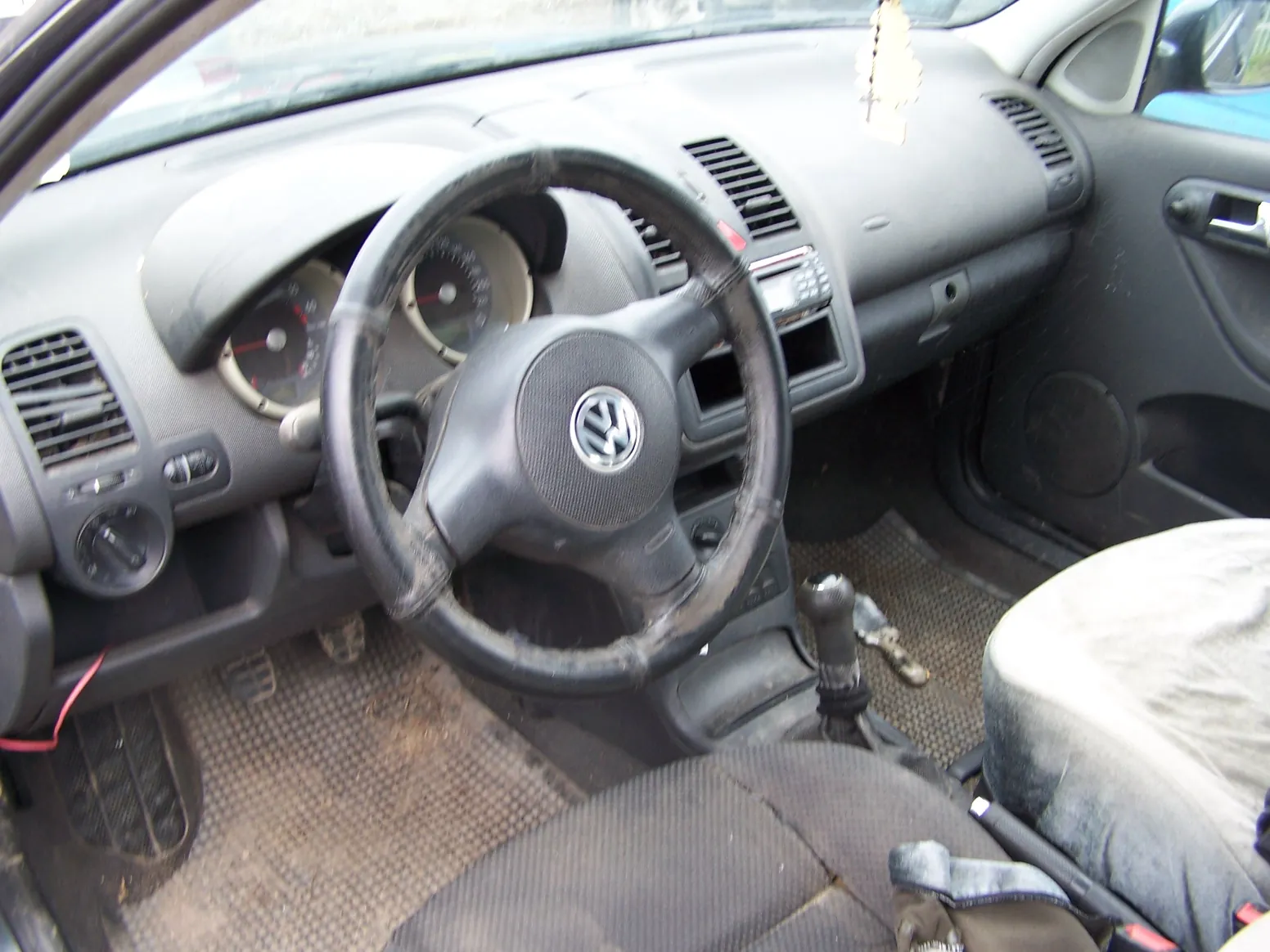 Wnętrze samochodu marki Volkswagen z widokiem na deskę rozdzielczą, kierownicę z logo VW, zegary oraz przednie fotele. Wnętrze jest zakurzone i w słabym stanie technicznym.