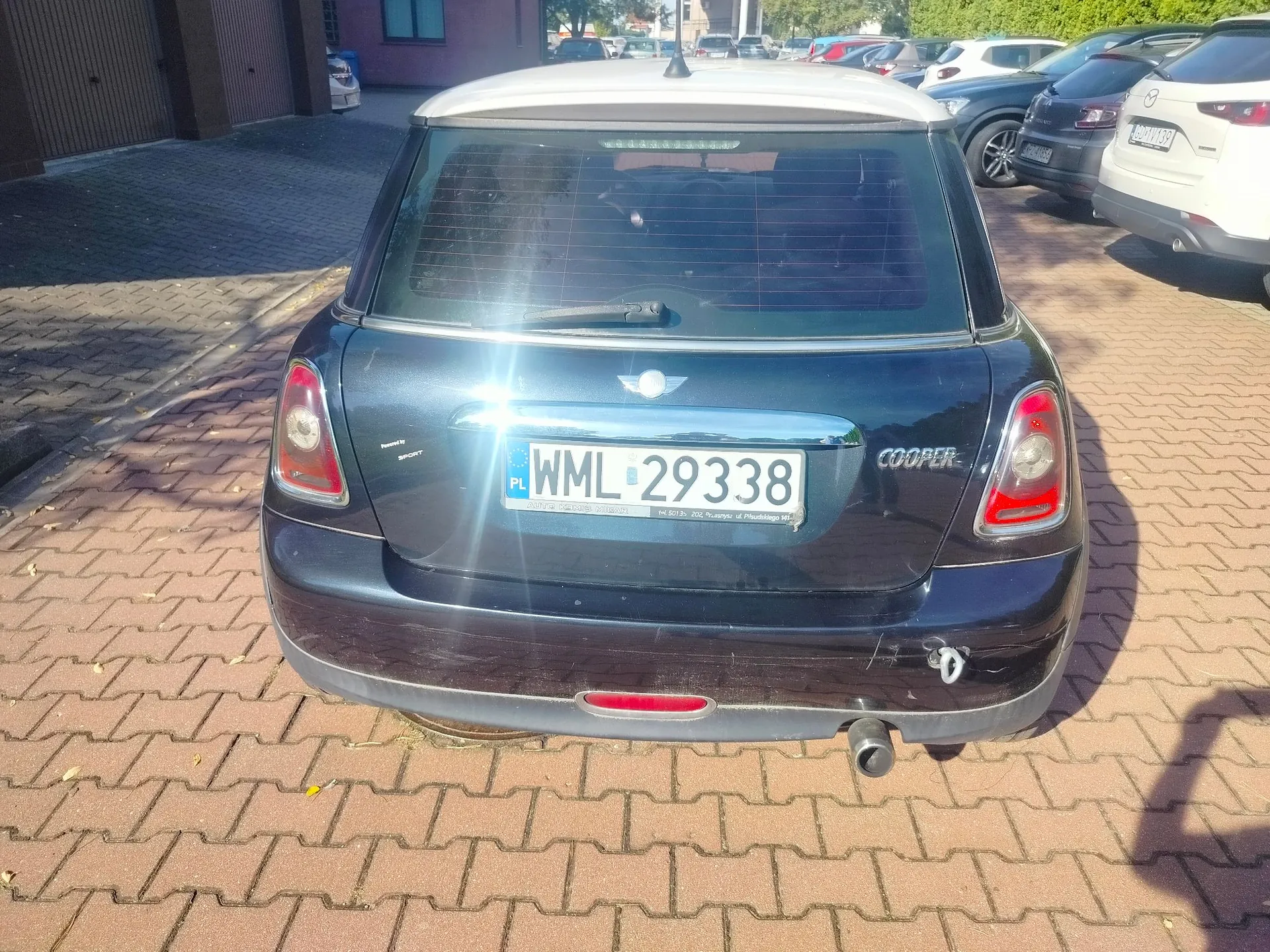 Tylny widok czarnego samochodu Mini Cooper zaparkowanego na kostce brukowej. Samochód ma biały dach i polską tablicę rejestracyjną o numerze WML 29338. Po prawej stronie klapy bagażnika widnieje napis COOPER, a nad tablicą rejestracyjną znajduje się logo marki Mini.