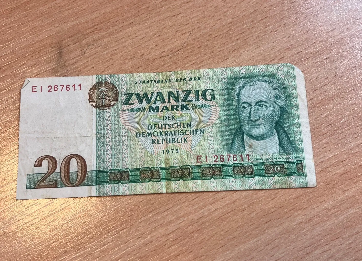 Banknot o nominale 20 marek z Niemieckiej Republiki Demokratycznej (NRD) z 1975 roku. Na banknocie widnieje portret mężczyzny po prawej stronie oraz napis 'ZWANZIG MARK DER DEUTSCHEN DEMOKRATISCHEN REPUBLIK'. W lewym górnym rogu i po prawej stronie znajduje się numer seryjny 'EI 267611'. W lewym dolnym rogu widoczna jest duża liczba '20'. Banknot leży na drewnianej powierzchni.