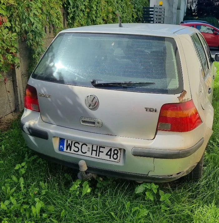 Srebrny samochód marki Volkswagen Golf w wersji TDI, widok od tyłu. Pojazd posiada polską tablicę rejestracyjną o numerze WSC HF 48. Samochód stoi na trawie przed zieloną ścianą z roślinności. Na tylnej klapie widoczne są napisy 'GOLF' oraz 'TDI' oraz logo Volkswagena. Po prawej stronie klapy widoczna jest niewielka rdza.