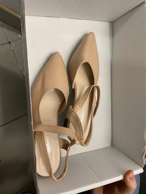 Para beżowych butów na obcasie z ostrymi czubkami i paskiem na kostce umieszczonych w białym pudełku. Buty mają gładką fakturę, a na wkładce widoczny jest napis 'Vizzano'. Pudełko trzyma ręka, w tle fragment podłogi z płytek.