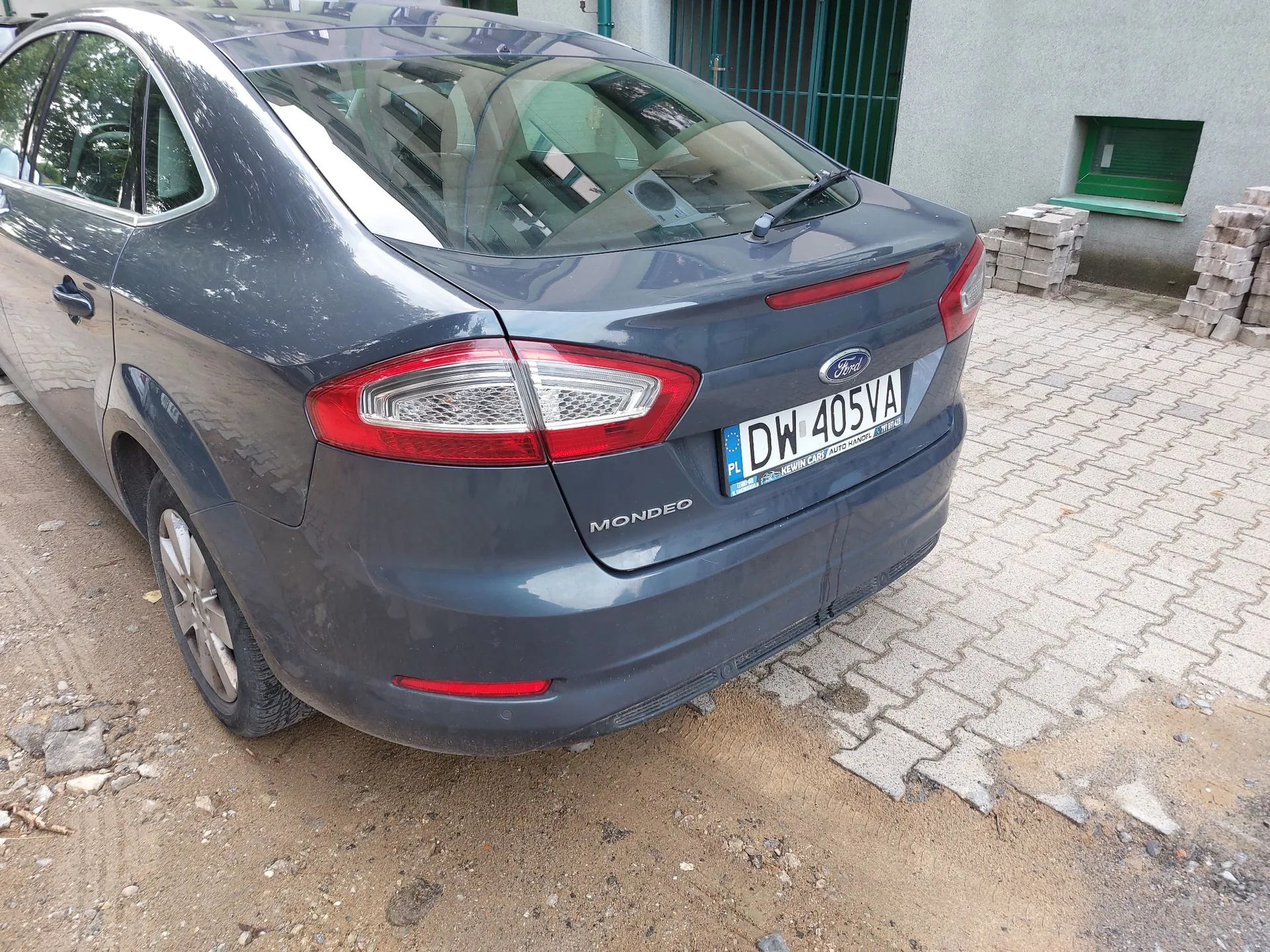 Tylny widok szarego samochodu marki Ford Mondeo zaparkowanego na kostce brukowej. Na samochodzie widoczna jest polska tablica rejestracyjna o numerze DW 405VA.