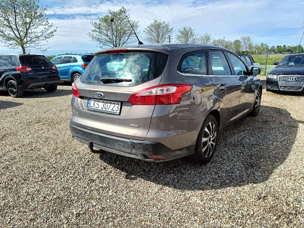 Szary samochód marki Ford w nadwoziu kombi zaparkowany na żwirowym placu. Widoczny jest tył i prawy bok pojazdu. Samochód posiada polską tablicę rejestracyjną o numerze LKS 30723. W tle znajdują się inne zaparkowane samochody oraz drzewa pod jasnym, lekko zachmurzonym niebem.