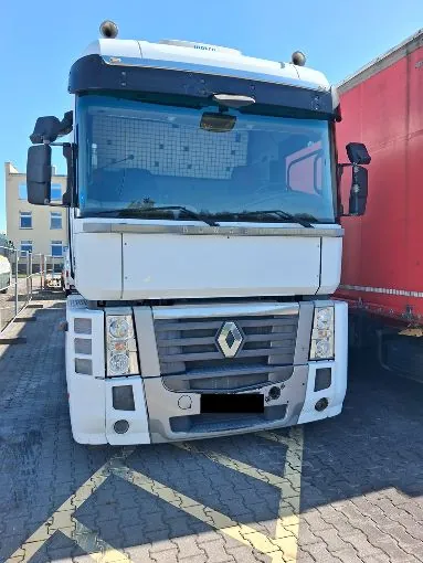 Widok z przodu białej ciężarówki marki Renault z czerwoną naczepą, zaparkowanej na kostce brukowej z żółtymi liniami wyznaczającymi miejsce postojowe.