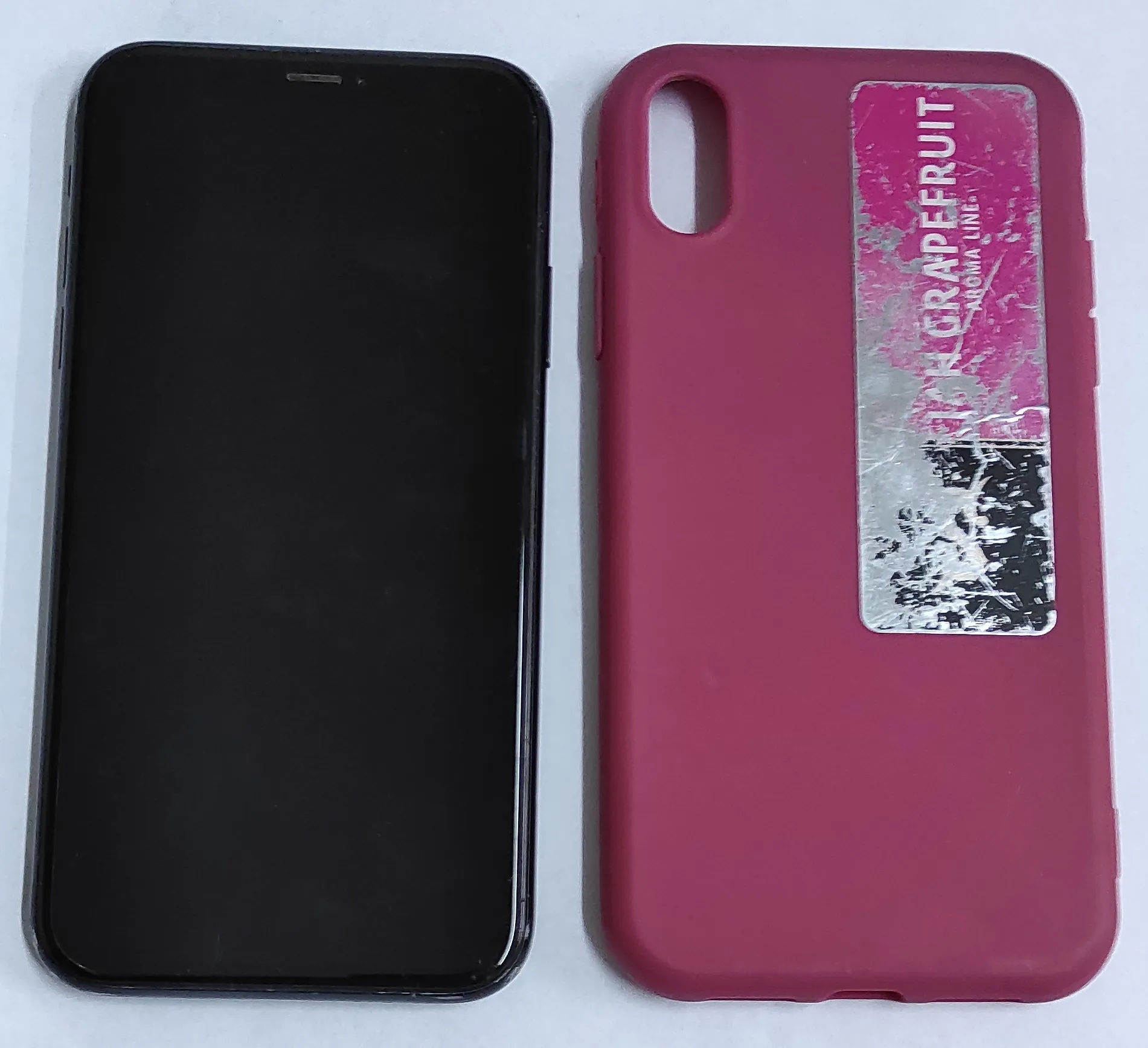 Obok siebie leżą dwa przedmioty: po lewej czarny smartfon z wyłączonym ekranem, a po prawej różowe etui ochronne na telefon. Na tylnej części etui znajduje się prostokątna naklejka z napisem „GRAPEFRUIT” oraz mniejszym tekstem „AROMA LINE” poniżej, na tle różowo-fioletowych i srebrnych plam.