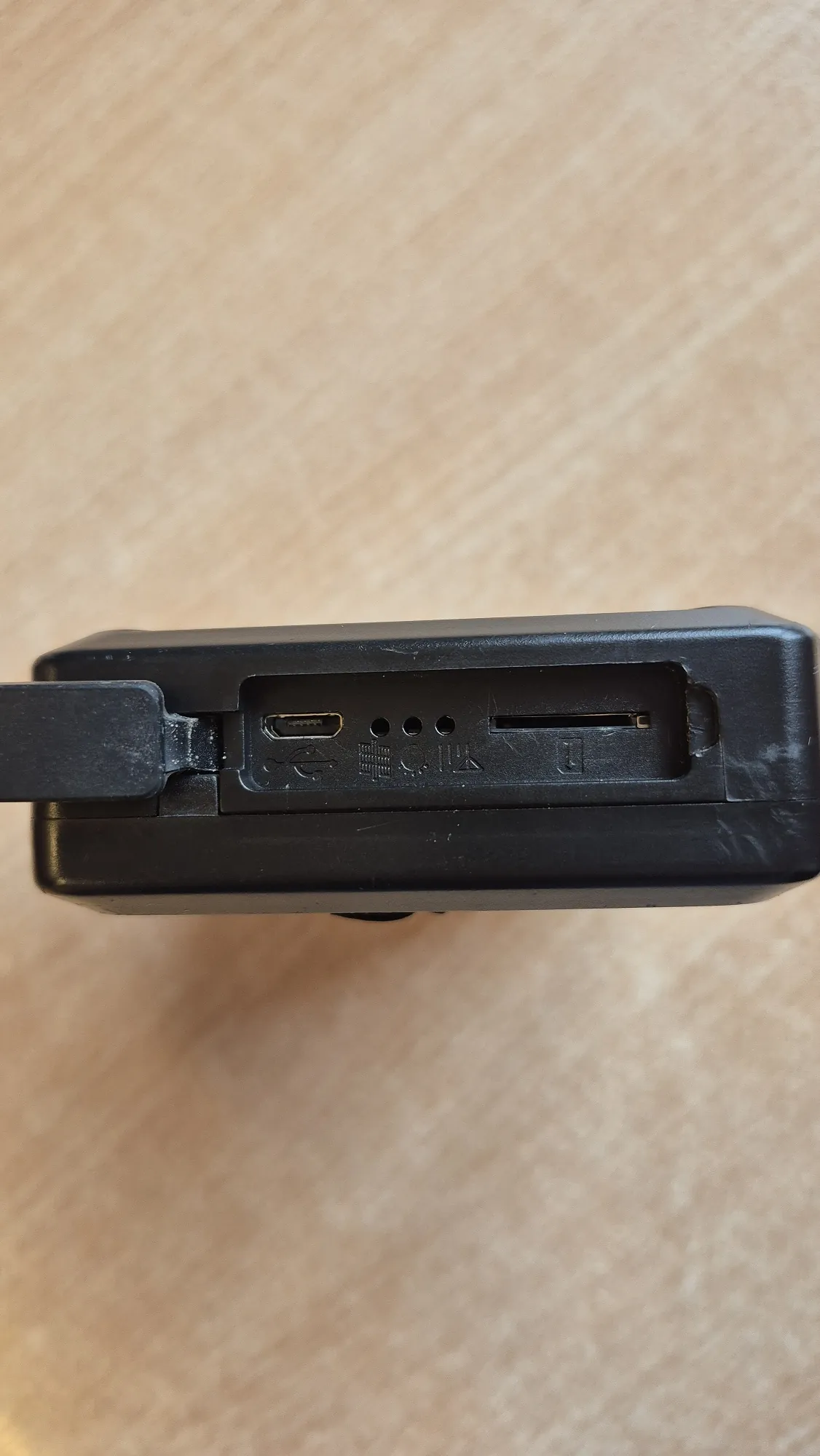 Zbliżenie na krawędź czarnego urządzenia elektronicznego. Widoczny jest port USB-C, trzy małe otwory mikrofonowe oraz gniazdo karty pamięci. Obok portów znajdują się wytłoczone symbole techniczne.