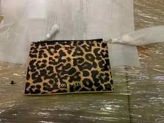 Portfel lub torebka w leoparдовym wzorze z widocznym tekstem 'DOLCE' na czarnym tle. Obiekt leży na powierzchni pokrytej przezroczystą folią.