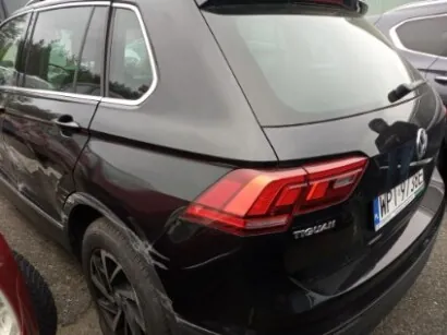 Czarny samochód typu SUV widziany od tyłu. Widoczny model 'Tiguan' oraz tablica rejestracyjna 'WP 12345'. W tle częściowo widoczny inny samochód. Samochód stoi na asfaltowej powierzchni.