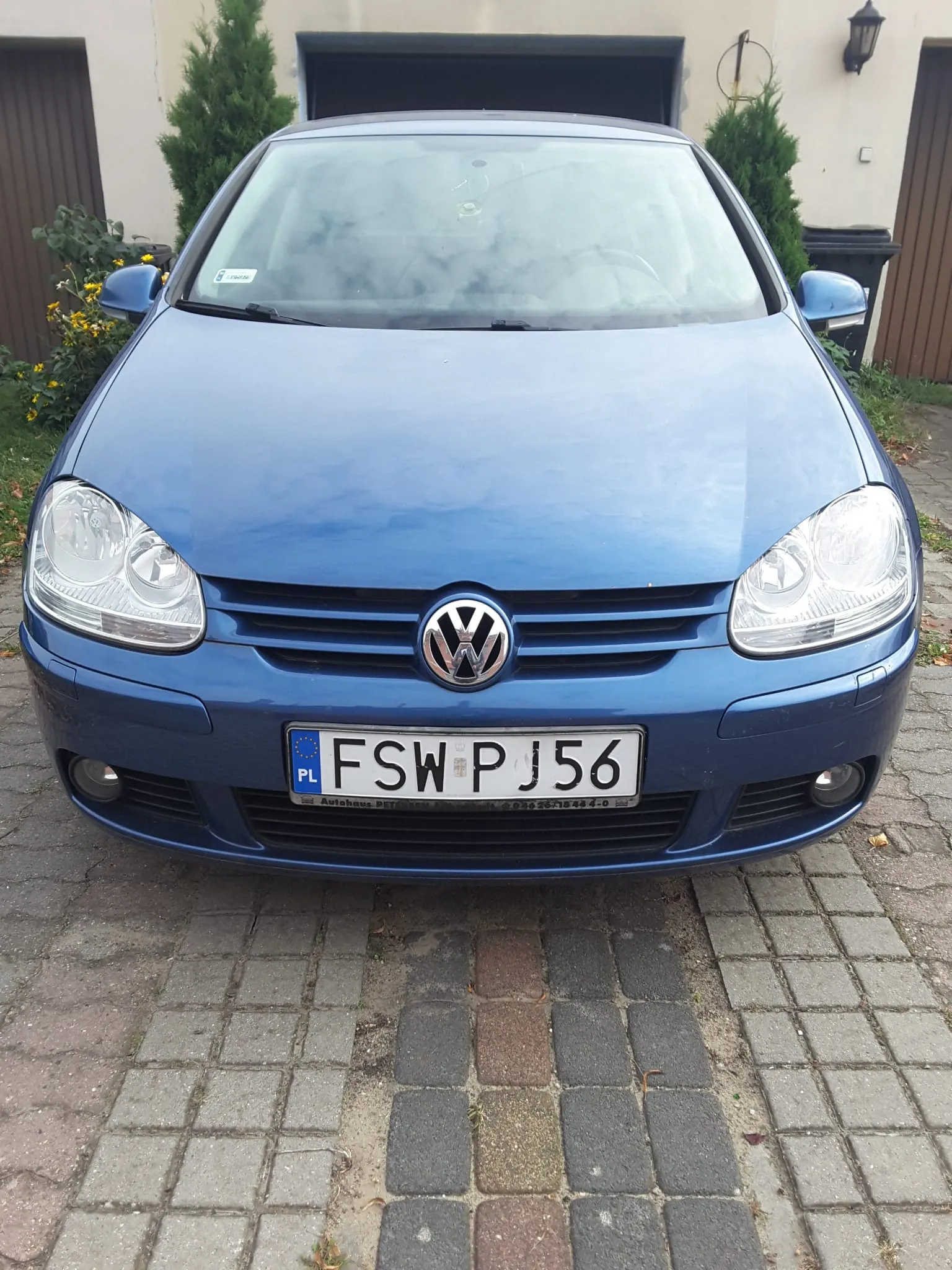 Niebieski samochód marki Volkswagen widziany od przodu, zaparkowany na kostce brukowej. Na samochodzie znajduje się polska tablica rejestracyjna o numerze FSW PJ56.