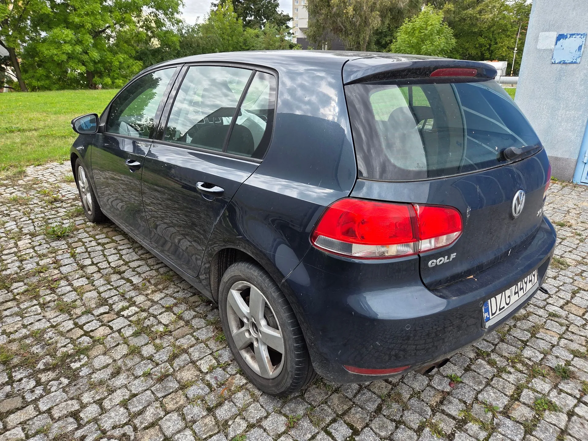 Ciemnoniebieski samochód marki Volkswagen Golf zaparkowany na kostce brukowej. Widok z tyłu i z boku pojazdu. Na klapie bagażnika widnieje napis GOLF oraz logo Volkswagena. Tablica rejestracyjna ma numer DZG 449Y.
