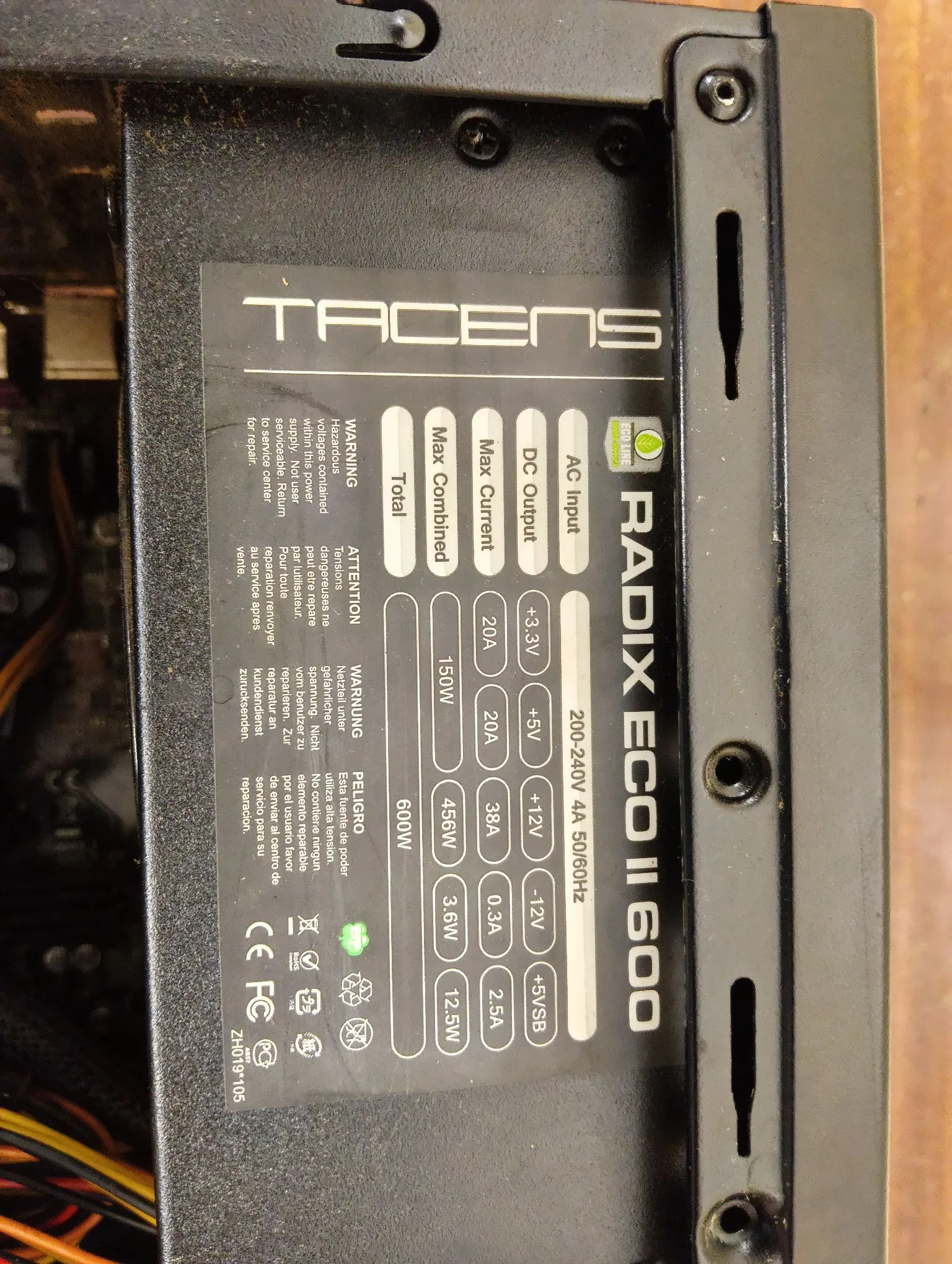 Zdjęcie z bliska etykiety technicznej zasilacza komputerowego marki Tacens, model Radix Eco II 600. Etykieta zawiera tabelę ze specyfikacją techniczną: AC Input: 200-240V 4A 50/60Hz; DC Output: +3.3V (20A), +5V (20A), +12V (38A, 456W), -12V (0.3A, 3.6W), +5VSB (2.5A, 12.5W). Max Combined Total: 150W dla linii 3.3V i 5V oraz 600W całkowitej mocy. Widoczne są również ostrzeżenia w kilku językach oraz certyfikaty CE i FCC.