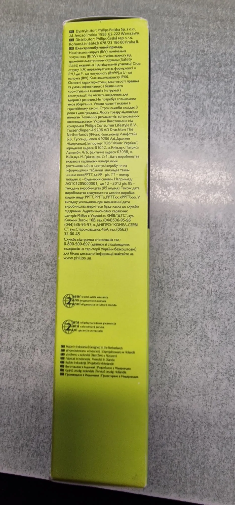 Zdjęcie fragmentu instrukcji obsługi lub opakowania produktu firmy Philips. Tekst jest napisany w języku polskim, czeskim i ukraińskim. Zawiera informacje o dystrybutorach w Polsce i Czechach, dane techniczne dotyczące zasilania, informacje o gwarancji oraz dane producenta. W dolnej części znajduje się zielony pasek z ikoną tarczy i napisem o gwarancji w kilku językach, m.in. 'Year world-wide warranty'. Na samym dole widnieje informacja o kraju pochodzenia: 'Made in Indonesia | Designed in the Netherlands' wraz z tłumaczeniami na inne języki.