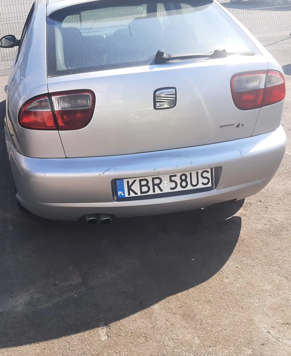 Tylny widok srebrnego samochodu marki SEAT. Na klapie bagażnika znajduje się logo producenta, a poniżej, na zderzaku, polska tablica rejestracyjna o numerze KBR 58US. Samochód ma dwa układy wydechowe po lewej stronie.