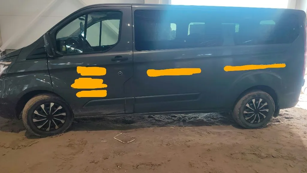 Profil ciemnoszarego vana zaparkowanego w pomieszczeniu o piaszczystej podłodze. Na boku pojazdu znajdują się pomarańczowe zakrycia w miejscach, gdzie prawdopodobnie znajdowały się napisy lub logo.