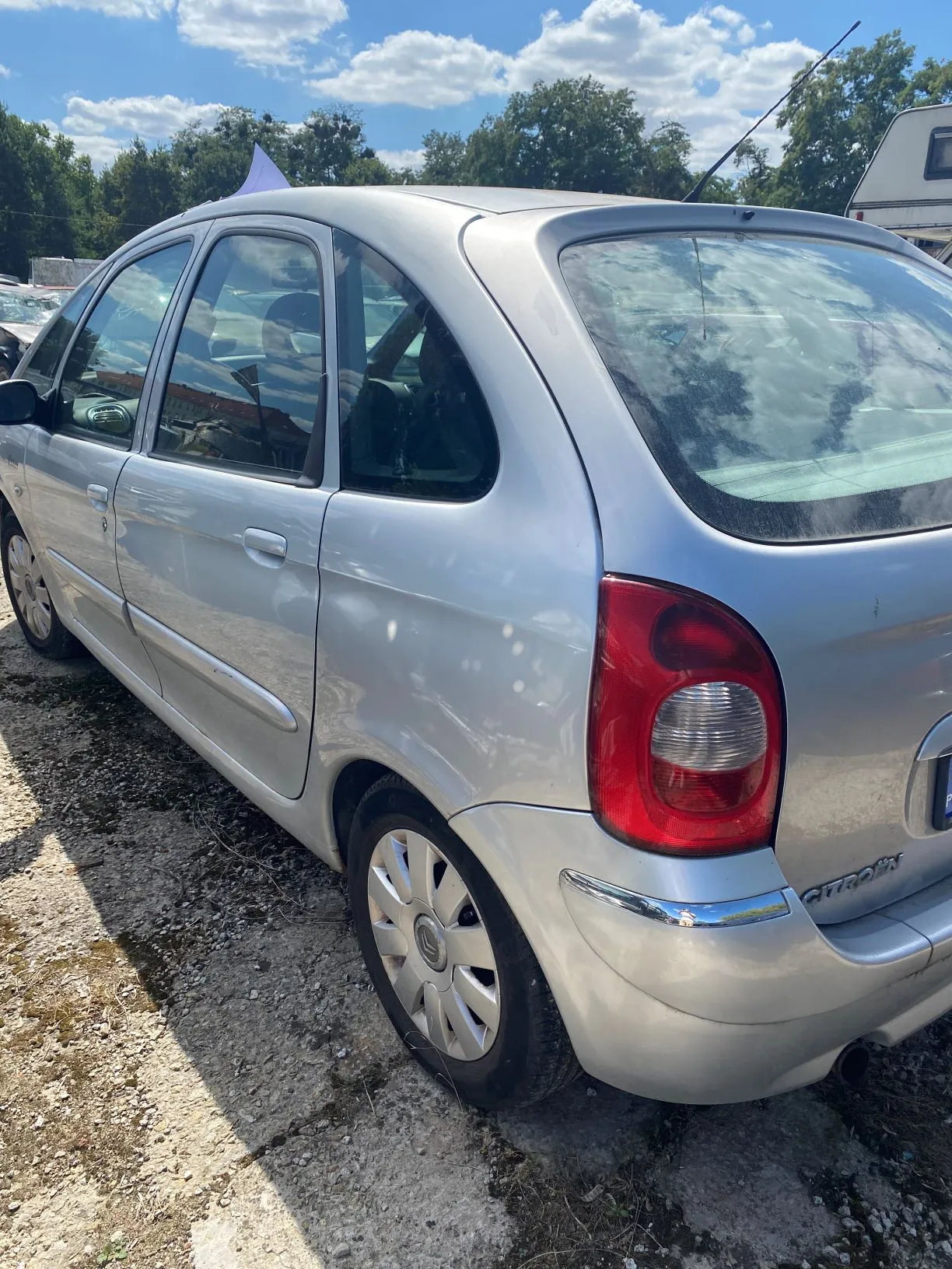 Srebrny samochód osobowy marki Citroën widziany z tyłu i z boku, zaparkowany na piaszczystym podłożu. Obraz jest obrócony o 90 stopni w lewo, przez co samochód znajduje się w pozycji pionowej.
