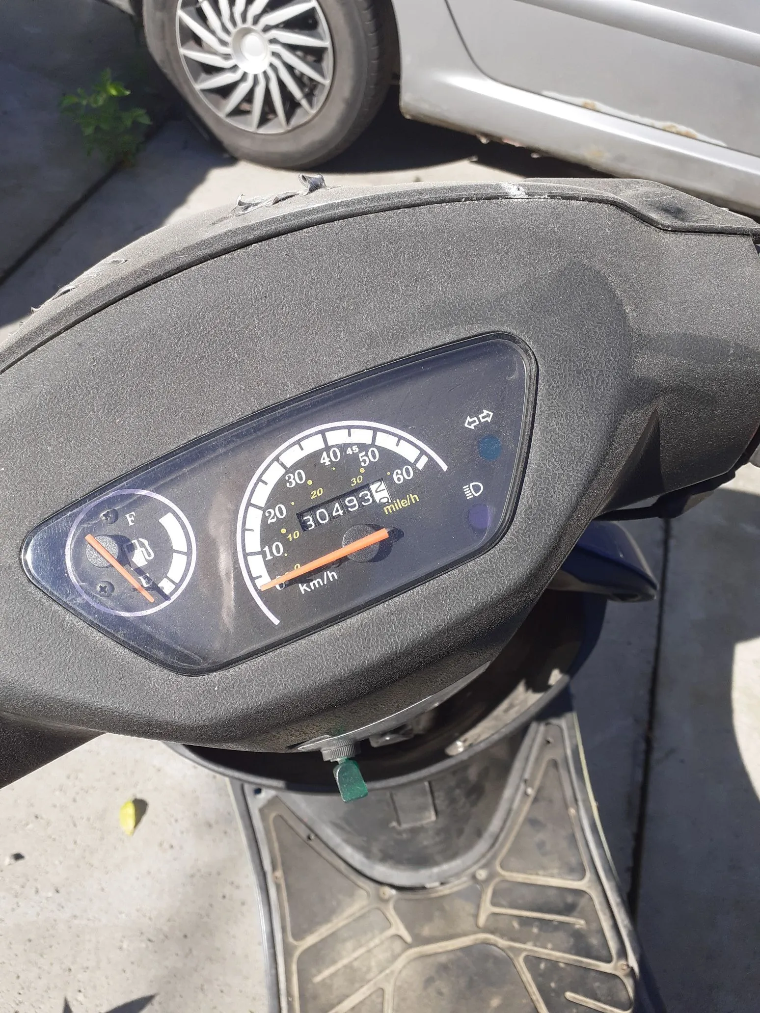 Zbliżenie na licznik prędkości skutera. Prędkościomierz wskazuje prędkość 0 km/h, a licznik kilometrów pokazuje wartość 30493. Na tarczy widoczne są oznaczenia prędkości od 0 do 60 km/h oraz wskaźnik poziomu paliwa (F). Obok licznika znajduje się napis 'mile/h'. Całość jest osadzona w czarnej, plastikowej obudowie skutera.