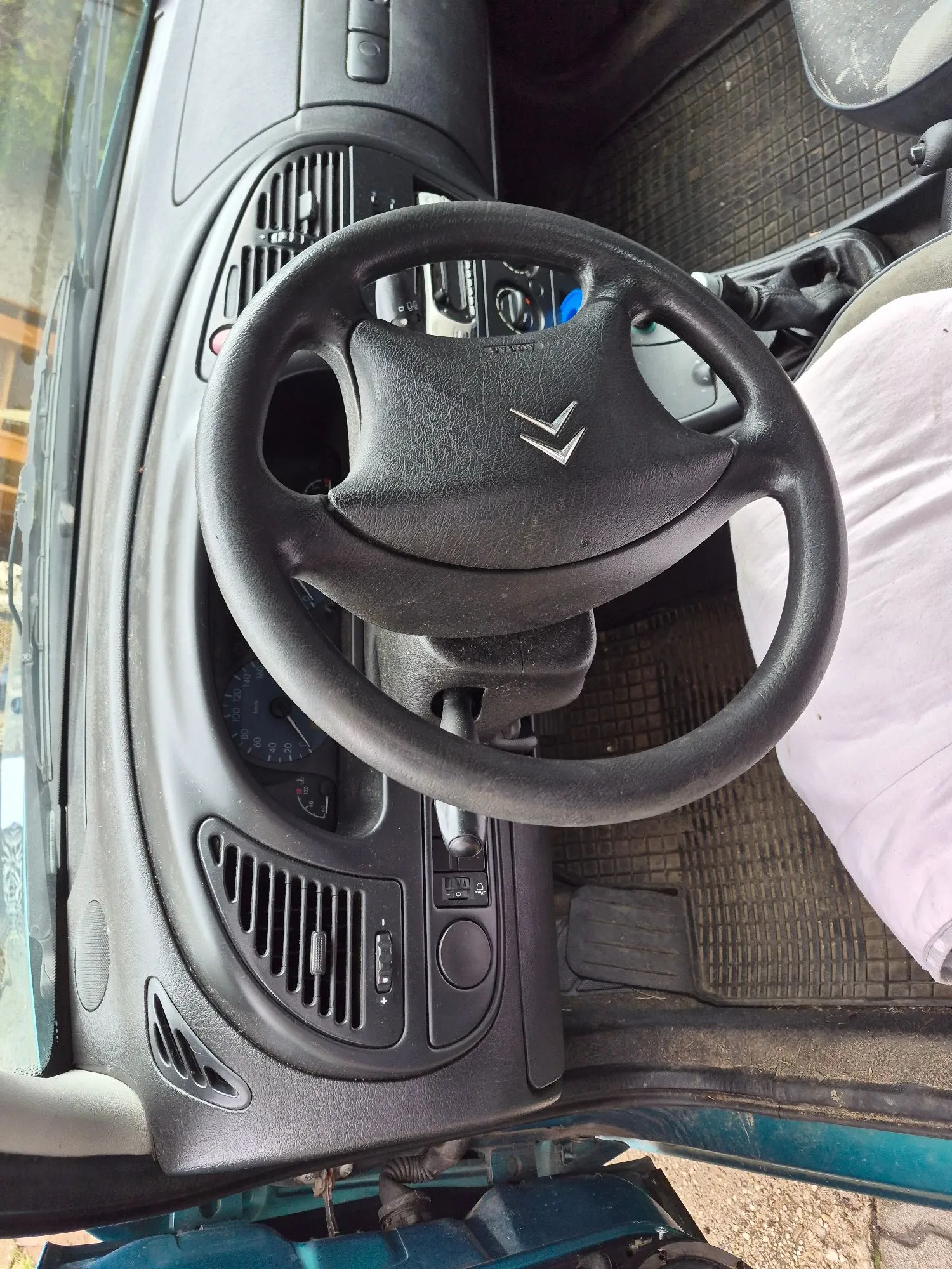 Wnętrze samochodu marki Citroën z widokiem na czarną kierownicę z logo producenta w centrum, deskę rozdzielczą z kratkami nawiewów oraz fragmenty podsufitki.