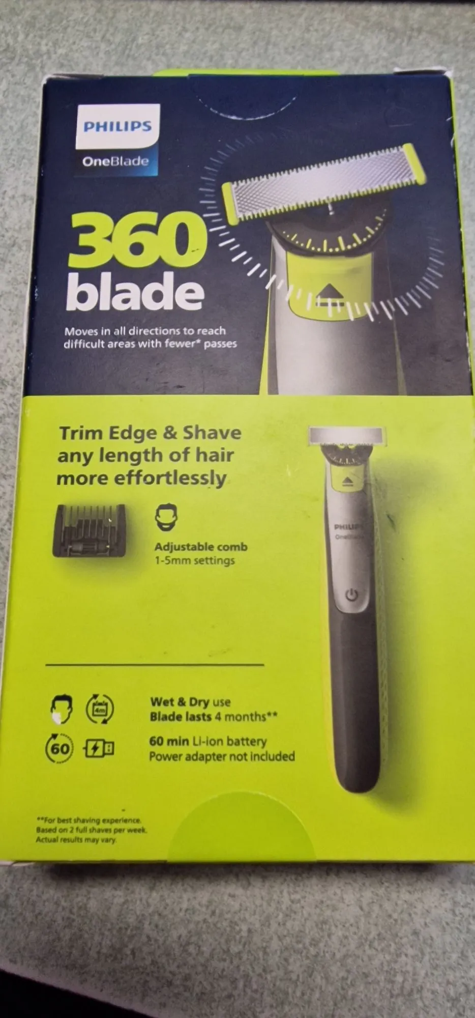 Opakowanie golarki Philips OneBlade 360 blade. Górna część pudełka jest ciemnoszara z napisem 'PHILIPS OneBlade 360 blade' oraz zdjęciem głowicy golarki. Poniżej znajduje się jasnozielona sekcja z tekstem 'Trim Edge & Shave any length of hair more effortlessly'. Widoczne są ikony i opisy funkcji: 'Adjustable comb 1-5mm settings', 'Wet & Dry use', 'Blade lasts 4 months**' oraz '60 min Li-ion battery Power adapter not included'. Po prawej stronie znajduje się zdjęcie całej golarki w kolorach szarym i limonkowym.