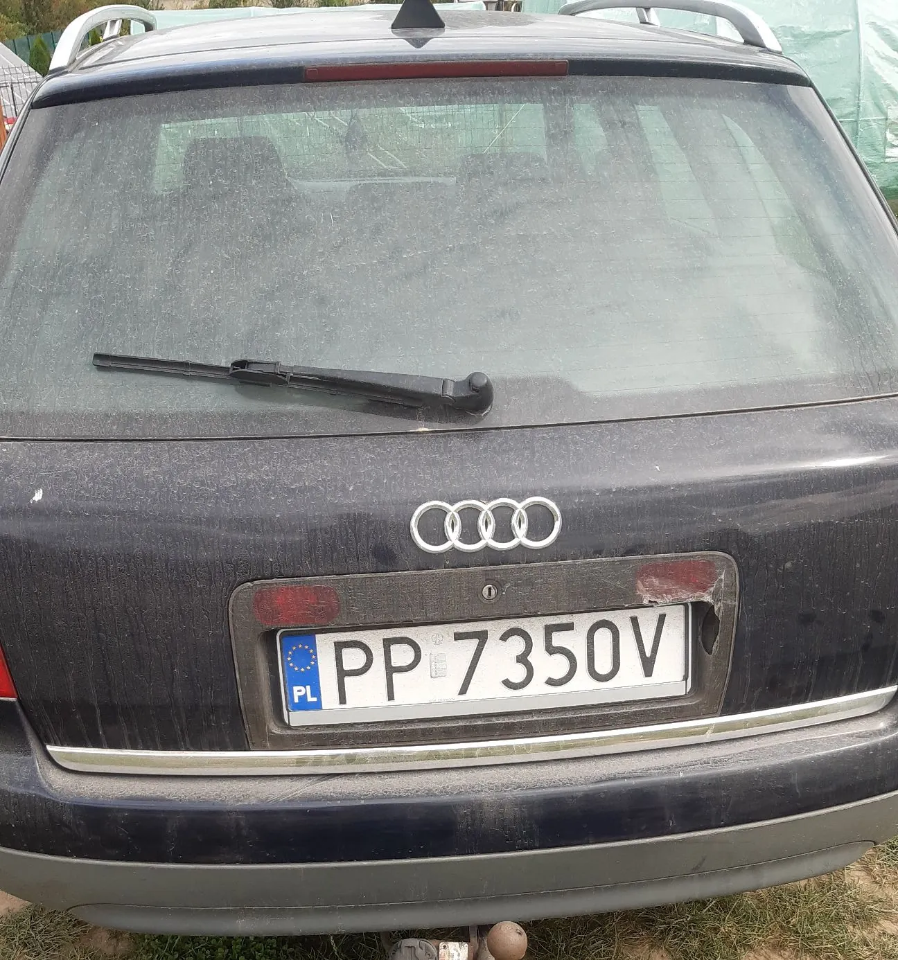 Tylny widok ciemnego, zakurzonego samochodu marki Audi. Na klapie bagażnika widoczne jest logo z czterema splecionymi pierścieniami oraz polska tablica rejestracyjna o numerze PP 7350V. Samochód posiada wycieraczkę tylnej szyby oraz relingi dachowe.