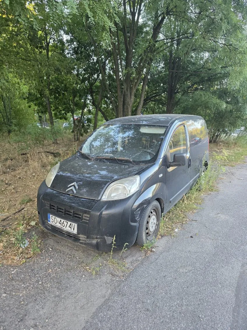 Czarny samochód dostawczy marki Citroën zaparkowany na poboczu drogi, w otoczeniu zielonych drzew i krzewów. Pojazd jest zakurzony, a na przednim zderzaku znajduje się polska tablica rejestracyjna o numerze SO 4674V.
