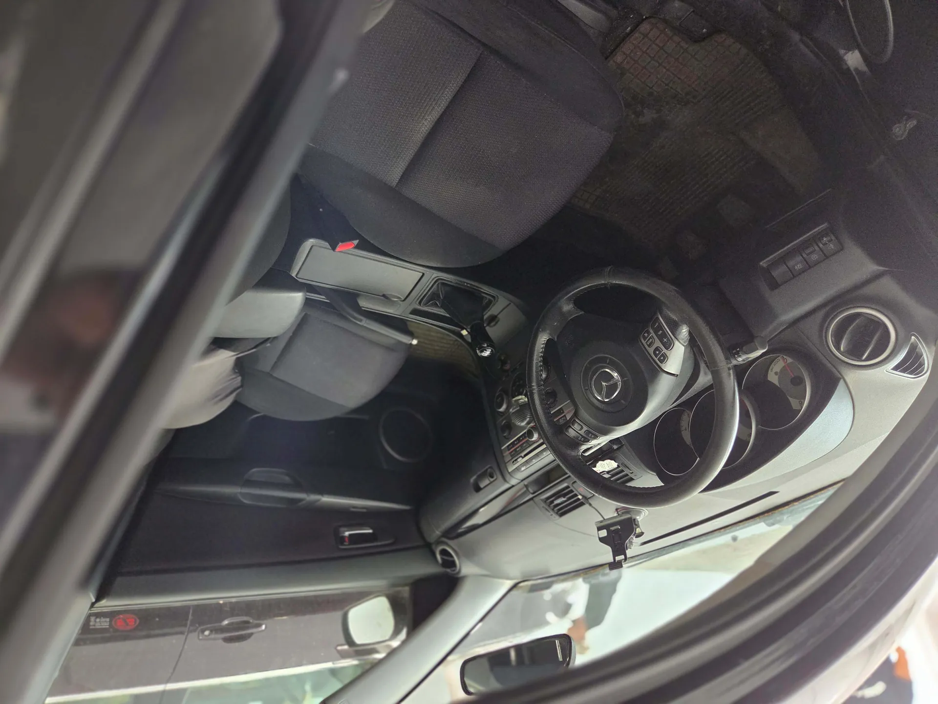 Wnętrze samochodu marki Mercedes-Benz widziane z perspektywy otwartych drzwi. Widoczna jest kierownica z logo marki, deska rozdzielcza, fotele oraz konsola środkowa. Obraz jest uchwycony pod dużym kątem, co powoduje silne zniekształcenie perspektywy.
