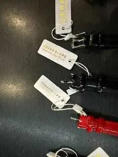 Trzy kluczniki w kolorach czerwonym i czarnym z białymi etykietami zawieszonymi na metalowych pierścieniach. Etykiety zawierają napis "100% LEATHER". Obiekty ułożone są na ciemnej powierzchni.