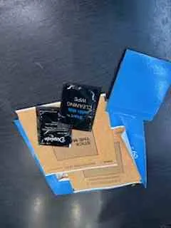 Brązowy kartonowy pakiet z niebieską taśmą, dwa czarne opakowania przekąsek z widocznym tekstem 'Doritos' oraz 'Cool Ranch', ułożone na ciemnej powierzchni.