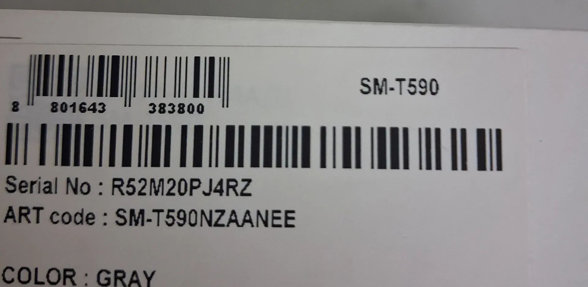 Zdjęcie etykiety produktowej z kodami kreskowymi i tekstem. W górnej części znajduje się kod kreskowy z numerami 8 801643 383800 oraz oznaczenie modelu SM-T590. Poniżej widnieje drugi, dłuższy kod kreskowy. Pod nim znajduje się tekst: 'Serial No : R52M20PJ4RZ', 'ART code : SM-T590NZAANEE' oraz na samym dole 'COLOR : GRAY'.