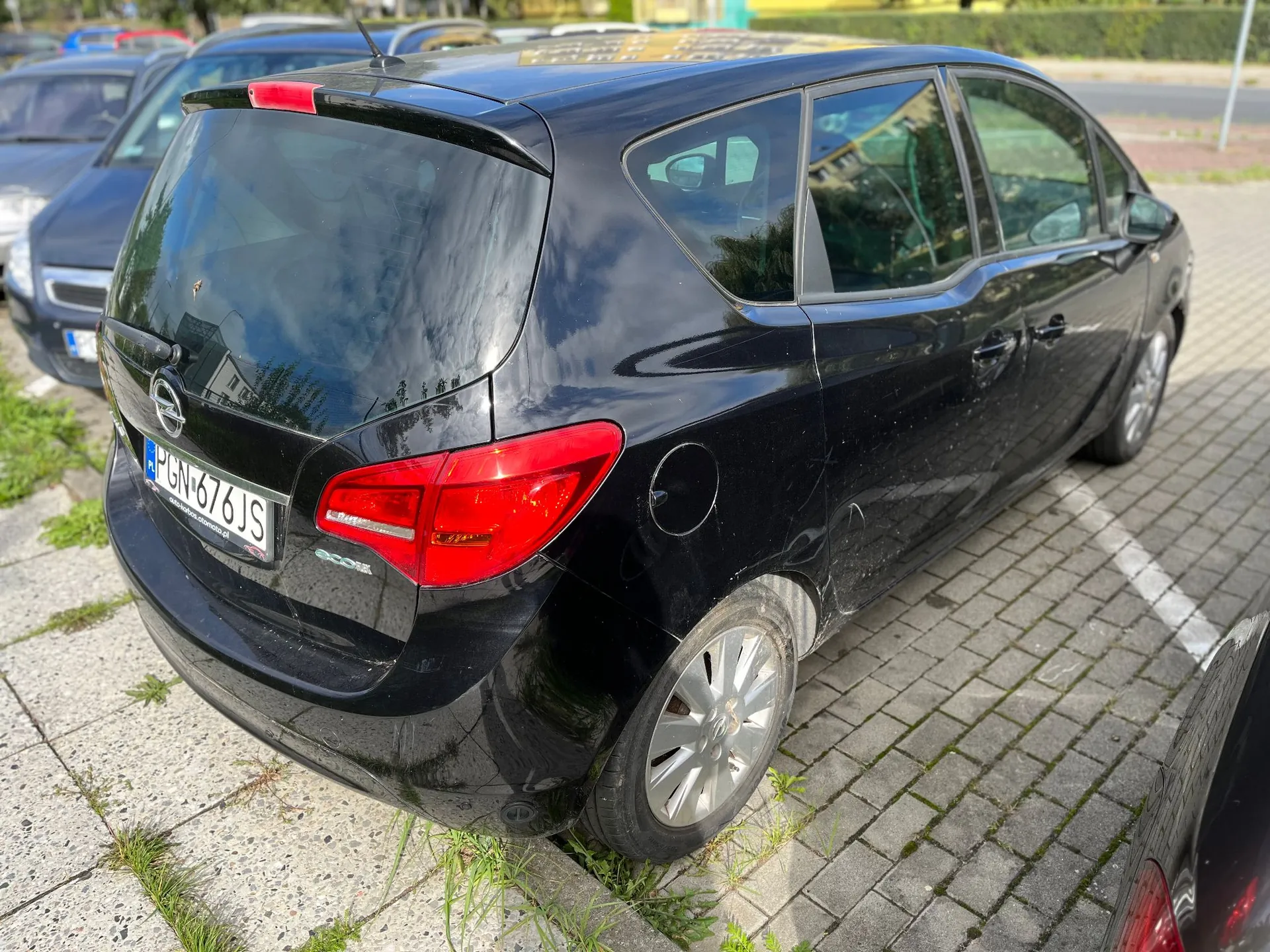 Czarny samochód marki Opel w nadwoziu kombi zaparkowany na kostce brukowej. Widoczny jest tył i prawy bok pojazdu. Samochód ma węgierską tablicę rejestracyjną o numerze PGN-676JS.