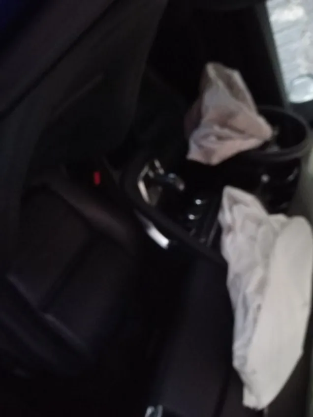 Wnętrze samochodu z rozwiniętymi poduszkami powietrznymi po stronie kierowcy i pasażera. Widoczne czarne skórzane fotele, kierownica, dźwignia zmiany biegów oraz deska rozdzielcza. Obraz jest nieostro wyeksponowany.