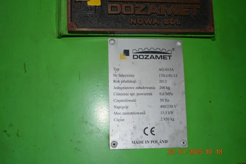 Srebrna tabliczka znamionowa przymocowana do zielonej obudowy urządzenia. Na górze znajduje się logo i napis 'DOZAMET'. Poniżej widnieją dane techniczne: Typ: AG-015A, Nr fabryczny: 170-1/01/13, Rok produkcji: 2013, Jednorazowe załadowanie: 200 kg, Ciśnienie spr. powietrza: 0,6 MPa, Częstotliwość: 50 Hz, Napięcie: 400/230 V, Moc zainstalowana: 15,5 kW, Ciężar: 2 850 kg. Na dole tabliczki widnieje znak CE oraz napis 'MADE IN POLAND'. Nad tabliczką znajduje się fragment ciemnej, metalowej tabliczki z napisem 'DOZAMET NOWA SÓL'. W prawym dolnym rogu zdjęcia widnieje data i godzina: 22.01.2025 10:18.