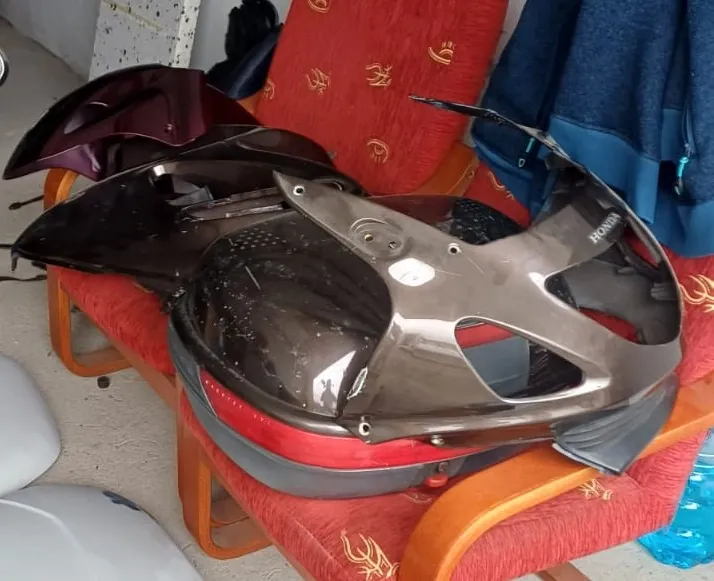 Części plastikowych owiewek motocyklowych w kolorze ciemnego brązu lub bordowym, ułożone na czerwonym fotelu z wzorami. Na jednej z części widoczny jest biały napis 'HONDA'.