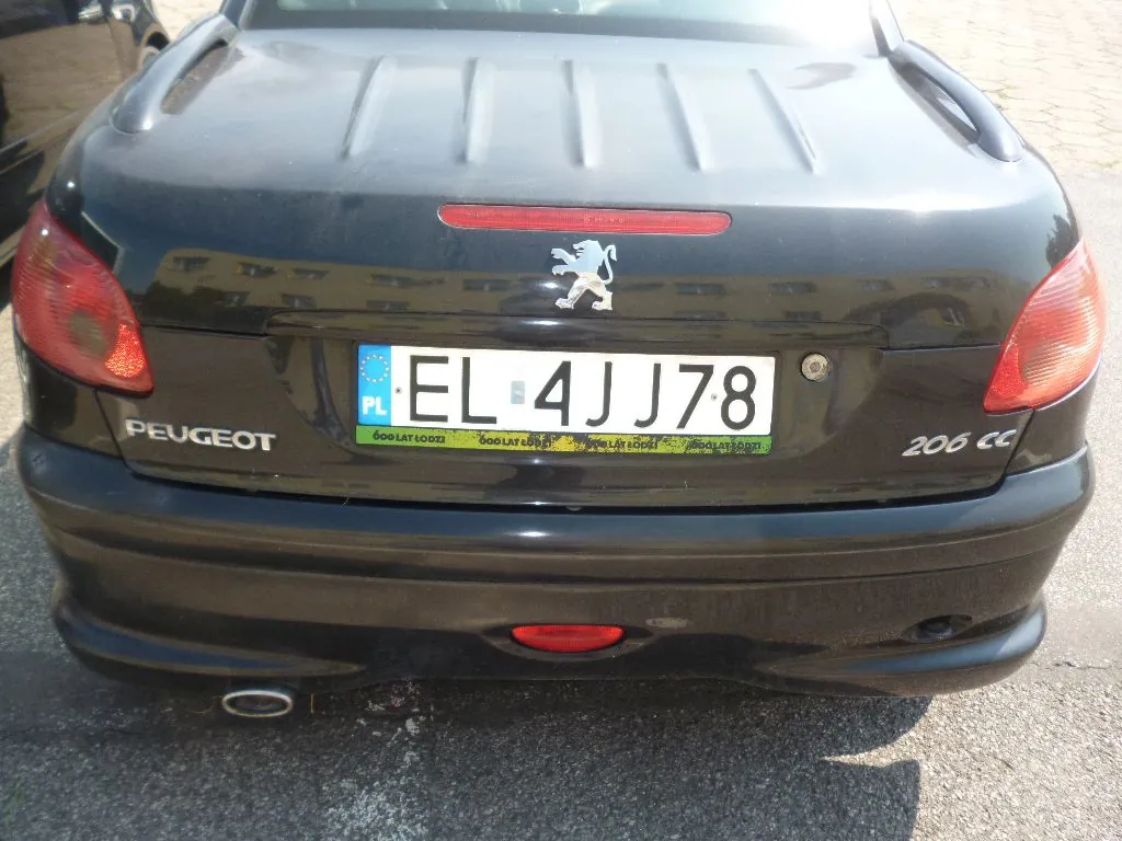 Tylny widok czarnego samochodu marki Peugeot 206 CC. Na klapie bagażnika znajduje się logo lwa Peugeot oraz polska tablica rejestracyjna o numerze EL 4JJ78 z niebieskim paskiem UE i oznaczeniem PL. Poniżej tablicy widnieje zielony pasek z powtarzającym się napisem '600 LAT ŁODZI'. Po lewej stronie znajduje się napis PEUGEOT, a po prawej 206 CC. Samochód ma czerwone tylne światła i widoczną rurę wydechową po lewej stronie.
