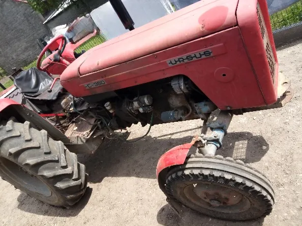 Czerwony traktor marki Ursus, model C-360, widoczny z profilu. Maszyna posiada duże tylne koło z charakterystycznym bieżnikiem oraz mniejsze przednie koło z błotnikiem. Na masce widoczne są napisy 'URSUS' oraz 'C-360'.
