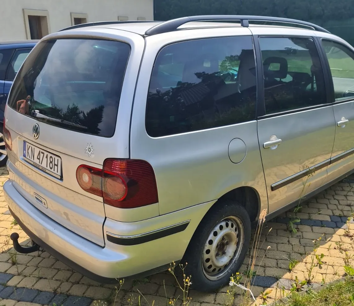 Srebrny samochód marki Volkswagen w nadwoziu kombi, zaparkowany na kostce brukowej. Widoczny jest tył oraz prawy bok pojazdu. Samochód posiada tablicę rejestracyjną o numerze KN 4718H, hak holowniczy oraz relingi dachowe. Na klapie bagażnika znajduje się logo Volkswagena oraz mała naklejka w kształcie słońca.