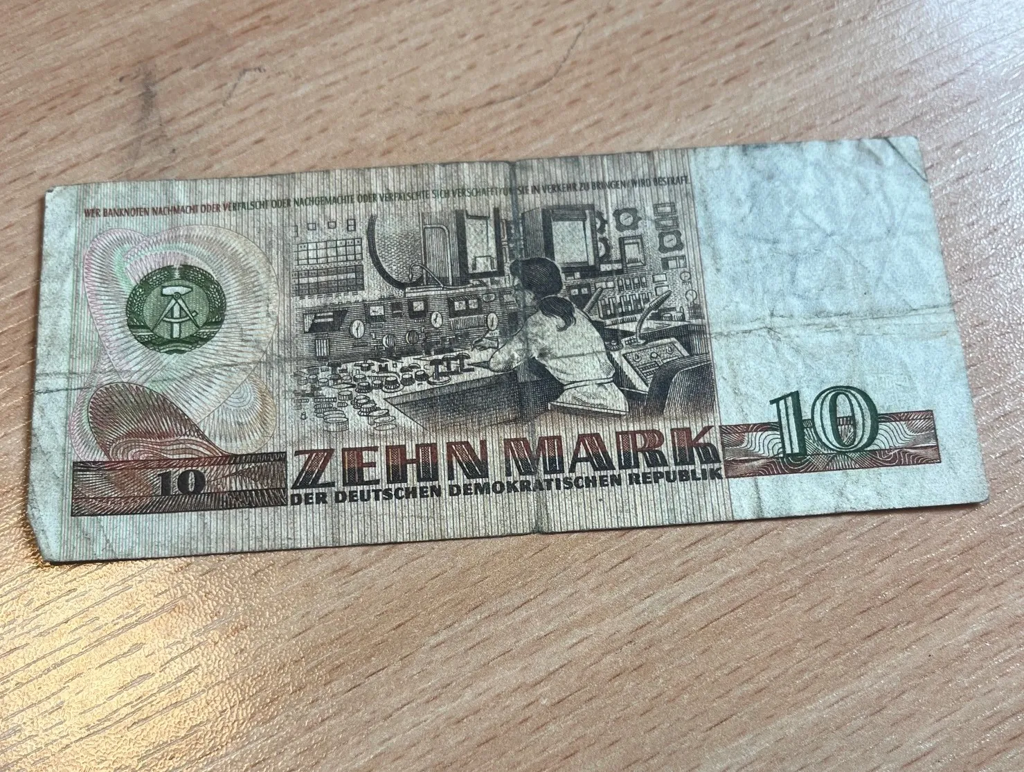Banknot o nominale 10 marek z Niemieckiej Republiki Demokratycznej (NRD). Na banknocie widnieje ilustracja osoby pracującej przy dużym panelu sterowania z licznymi przyciskami i wskaźnikami. W dolnej części znajduje się napis 'ZEHN MARK' oraz mniejszym drukiem 'DER DEUTSCHEN DEMOKRATISCHEN REPUBLIK'. Po lewej stronie widoczny jest godło NRD w okręgu, a po prawej oraz lewej stronie liczba '10'.