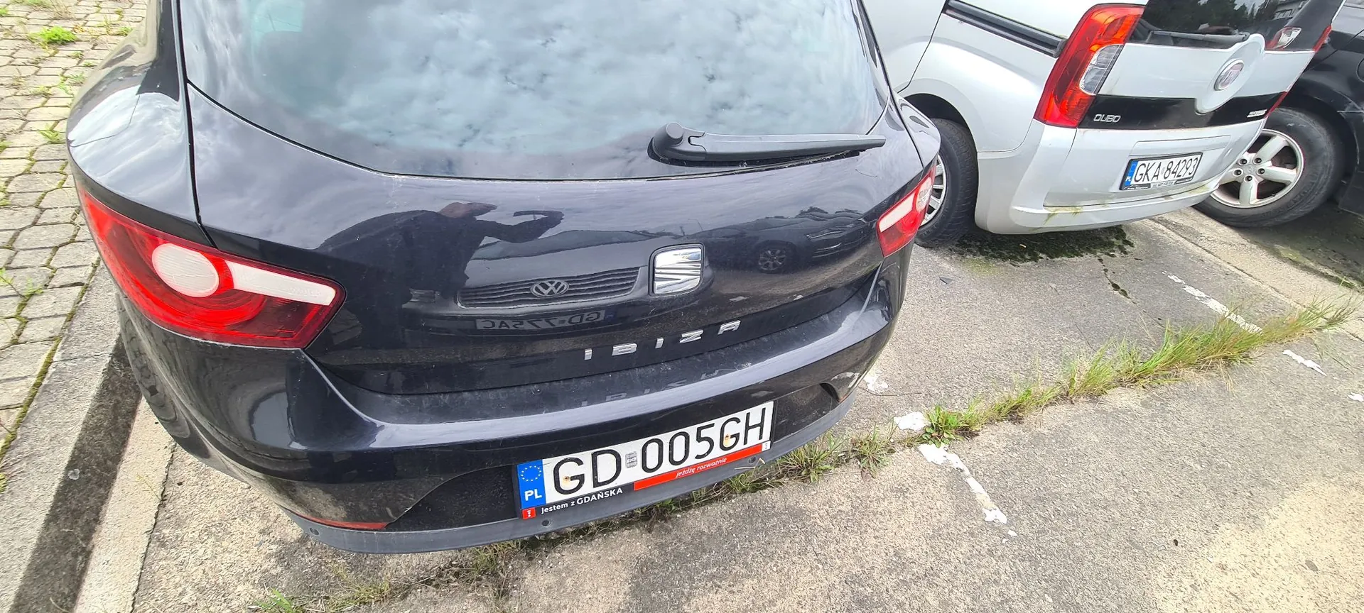 Tylny widok czarnego samochodu marki Seat Ibiza zaparkowanego na betonowym placu. Na samochodzie widoczna jest polska tablica rejestracyjna o numerze GD 005GH z napisem 'jestem z GDAŃSKA'. Obok stoi biały samochód z tablicą rejestracyjną GKA 84293.