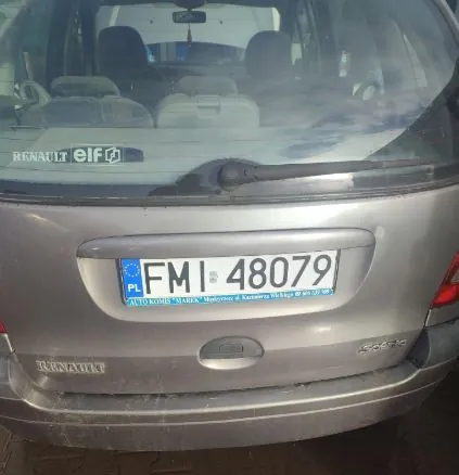 Tył srebrnego samochodu marki Renault z widoczną tablicą rejestracyjną PL FM 48079. Na szybie tylnej naklejka z napisem RENAULT elf. Widoczne siedzenia wewnątrz pojazdu oraz logo RENAULT na bagażniku.