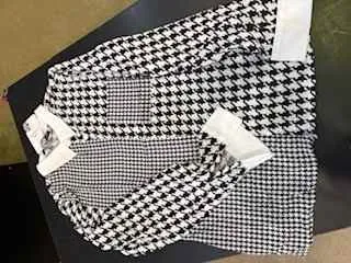 Czarno-biała tkanina w wzór houndstooth, prawdopodobnie część ubrania, ułożona na ciemnej powierzchni. Widoczne są białe etykiety przyszyte do tkaniny.