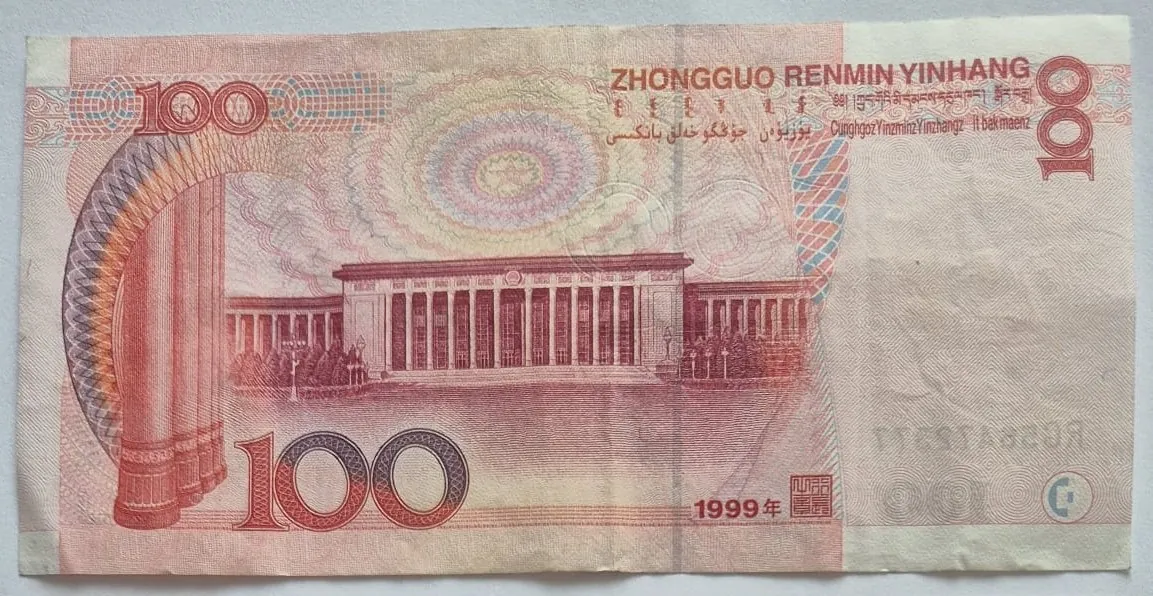 Chiński banknot o nominale 100 juanów w kolorystyce czerwonej i różowej. W centralnej części znajduje się wizerunek budynku z kolumnadą. W górnej części widnieje napis 'ZHONGGUO RENMIN YINHANG' oraz teksty w innych językach. Liczba '100' pojawia się w trzech miejscach: w lewym górnym rogu, prawym górnym rogu oraz dużym drukiem w lewym dolnym rogu. W prawym dolnym rogu widnieje data '1999年'.