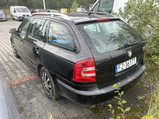 Czarny samochód marki Skoda w nadwoziu kombi zaparkowany na kostce brukowej. Widoczny jest tył i lewy bok pojazdu. Samochód ma tablicę rejestracyjną o numerze FZ 3617T. W tle widoczne są inne pojazdy, w tym biały furgon, oraz zielone krzewy.
