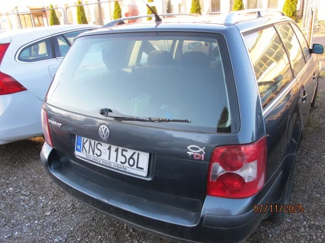 Tylny widok ciemnoszarego samochodu osobowego marki Volkswagen kombi z tablicą rejestracyjną KNS-1156L i oznaczeniem TDI. Po lewej stronie widoczny biały samochód. Tło stanowią budynki i zielone krzewy. Na dole po prawej stronie widoczna data 07/11/2025. Samochód zaparkowany na żwirowym podłożu.