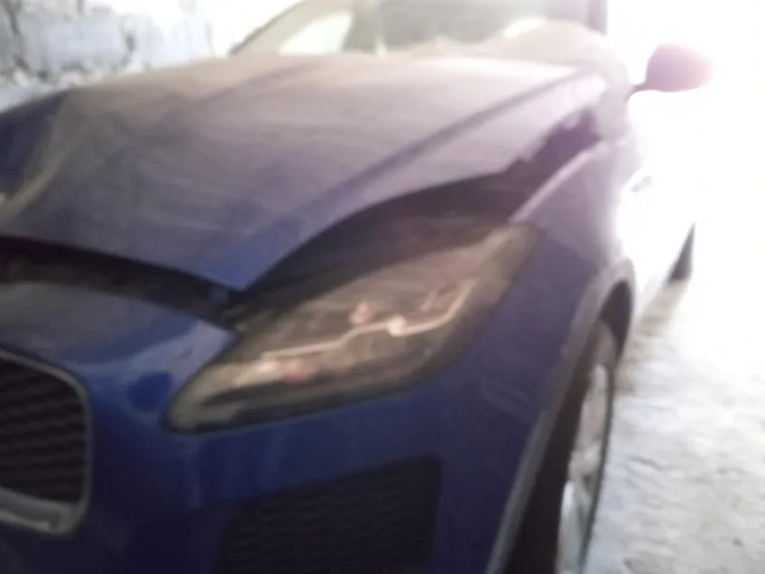 Niebieski samochód widziany od przodu, z widocznym reflektorem, atrapą chłodnicy i częścią koła. Tło pokryte śniegiem lub lodem.