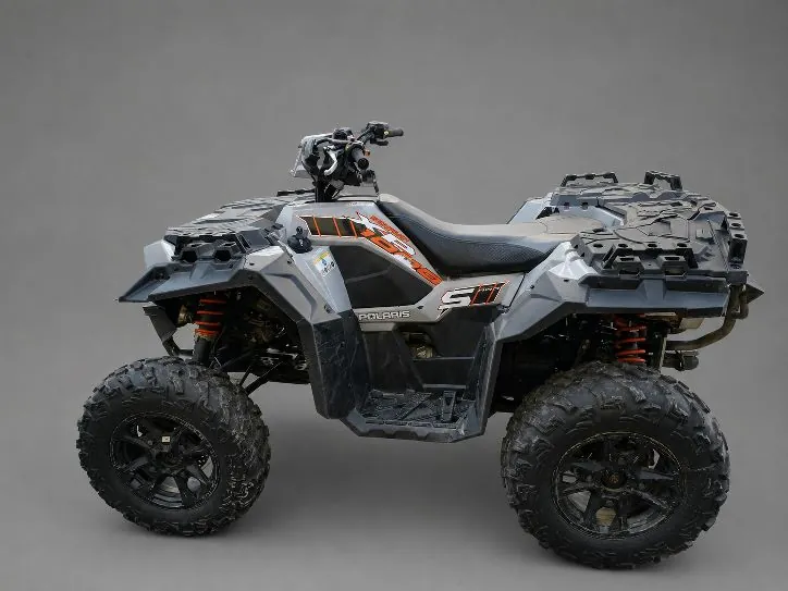 Szary quad marki Polaris z pomarańczowymi akcentami, zaprezentowany z profilu na jednolitym, szarym tle. Pojazd posiada duże, terenowe opony z głębokim bieżnikiem, widoczne czerwone sprężyny amortyzatorów oraz napis 'POLARIS' i logo '500' na boku obudowy.