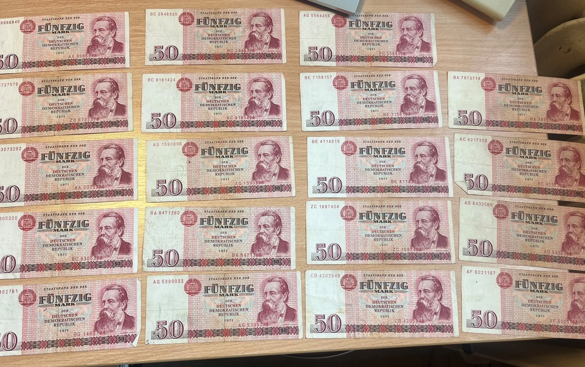 Kolekcja banknotów o nominale 50 marek z Niemieckiej Republiki Demokratycznej (NRD), ułożonych w pięciu rzędach i czterech kolumnach. Banknoty mają różowy kolor i przedstawiają portret mężczyzny z brodą po prawej stronie. Na każdym banknocie widnieje napis 'FÜNFZIG MARK' oraz 'STAATSBANK DER DDR'.
