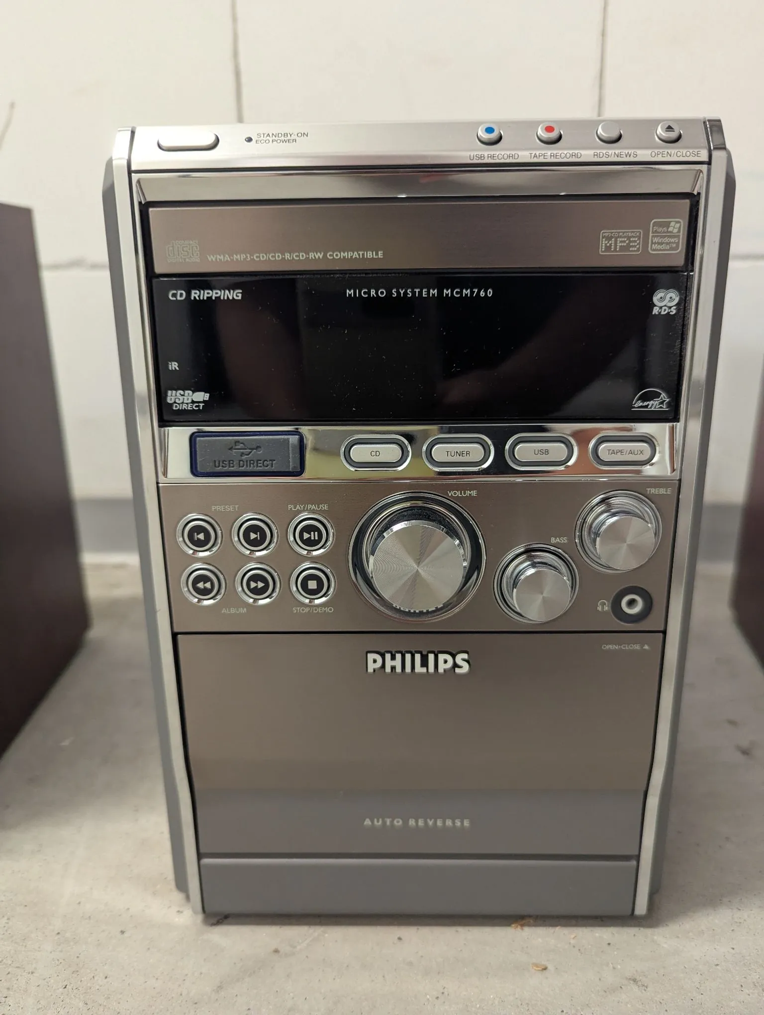 Srebrny zestaw muzyczny marki Philips, model Micro System MCM760. Urządzenie posiada wyświetlacz LCD, odtwarzacz CD, port USB oraz liczne przyciski sterujące i pokrętła do regulacji głośności, basu i tonów wysokich. Na obudowie widoczne są napisy: 'WMA-MP3-CD/CD-R/CD-RW COMPATIBLE', 'CD RIPPING', 'USB DIRECT' oraz 'AUTO REVERSE'.