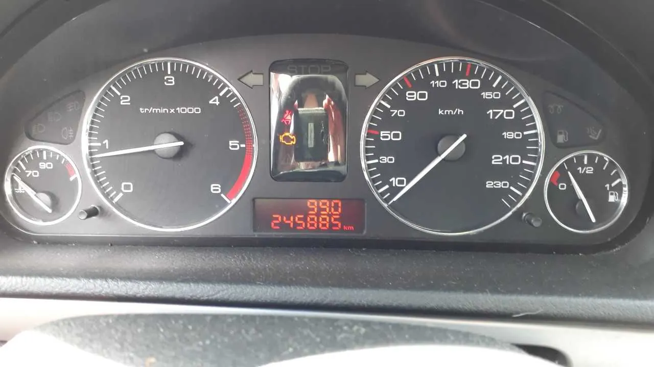 Tablica przyrządów samochodowych z czarnym tłem. Po lewej stronie mały wskaźnik (prawdopodobnie temperatury chłodniczki) z zakresem 70-90. Obok niego większy tachometr z zakresem 0-6 (oznaczony jako tr/min x1000), wskazujący około 1. W centrum wyświetlacz z napisem STOP, żółtym symbolem lampy ostrzegawczej oraz cyfrowym licznikiem przebiegu 245885 km i wartością 990. Po prawej stronie prędkościomierz z zakresem 0-230 km/h (wskazujący 0) oraz wskaźnik paliwa pokazujący poziom poniżej 1/2. Wszystkie skale i napisy są czytelne, bez obrócenia.